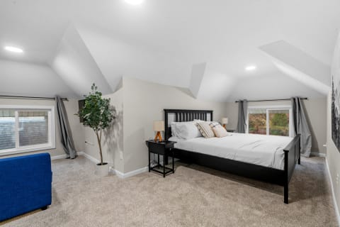 Cozy attic bedroom with slanted ceiling, bed, blue sofa, and a plant.