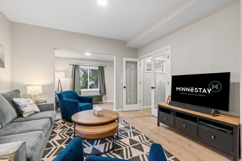 Cozy living room featuring a grey sofa, blue armchairs, and a stylish coffee table with a television displaying the MINNESTAY logo.
