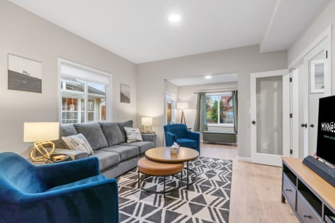 A modern living room featuring a grey sofa, blue armchairs, and large windows with natural light.