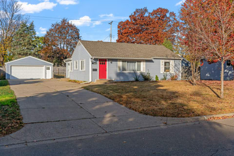 Single-story blue house with a red front door and autumn foliage.