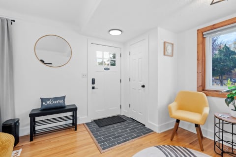 Bright entryway with a wooden bench, yellow chair, and decorative mirror against white walls.