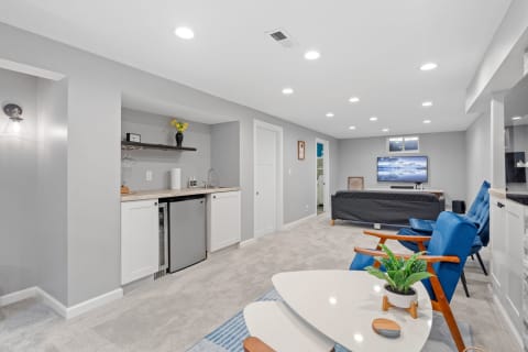 A stylish basement living room with a bar area, blue chairs, and a large television.