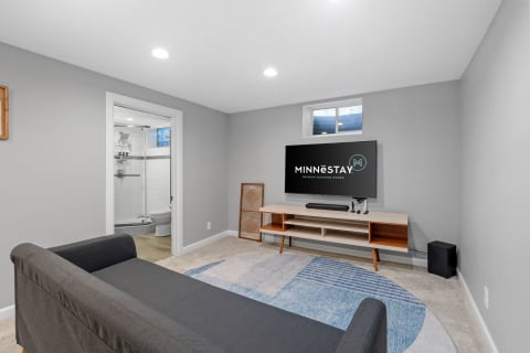 Modern living room with a dark gray sofa, wall-mounted TV, and a view of a bathroom.