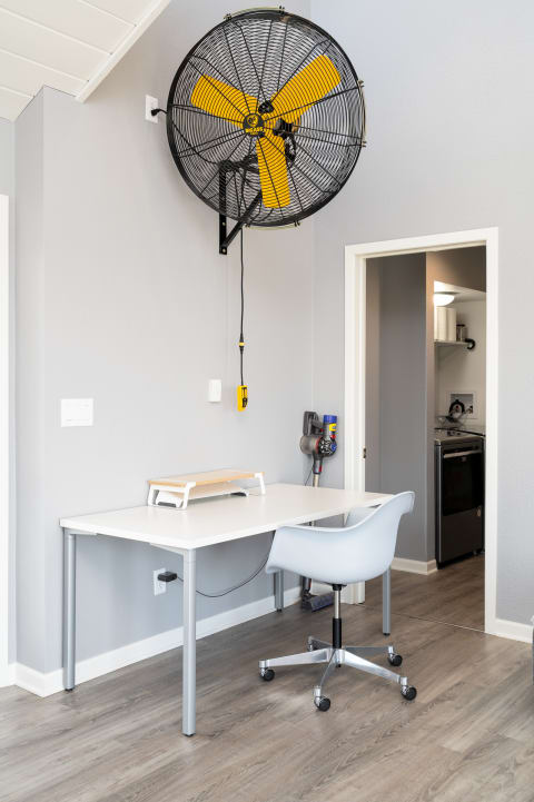 Modern workspace with white table, grey chair, and wall-mounted fan.