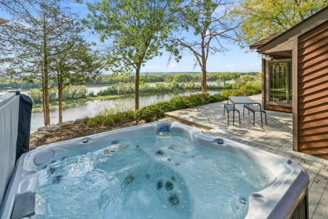 Outdoor hot tub on a wooden deck with a view of a river and lush greenery.