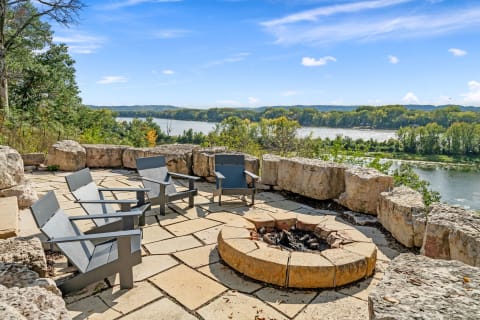 Outdoor seating area with modern chairs and a stone fire pit by the river.