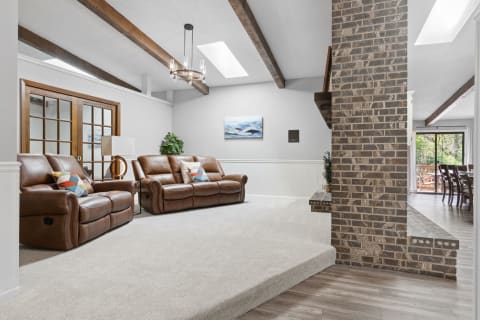 Spacious living room featuring leather recliners, wooden beams, and large windows.