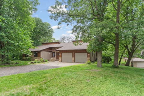 A beautiful single-family home with a sloping drive and dense trees surrounding it.