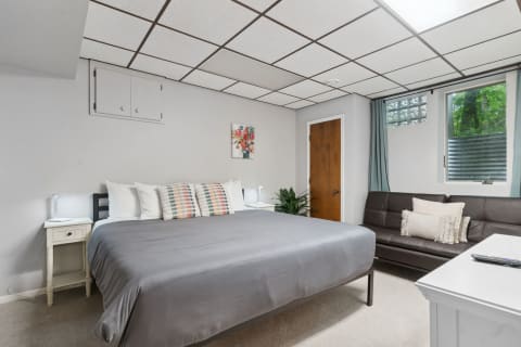 A comfortable bedroom with a large gray bed, colorful pillows, and a leather sofa.