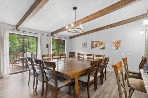 Dining room featuring a large table, wooden beams, and soft gray walls with art.