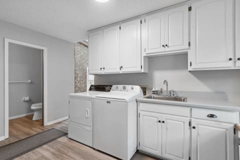 Interior view of a laundry room featuring a washer, dryer, and sink beneath white cabinets.