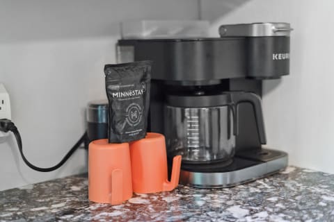A modern coffee station with orange mugs and a black coffee maker.