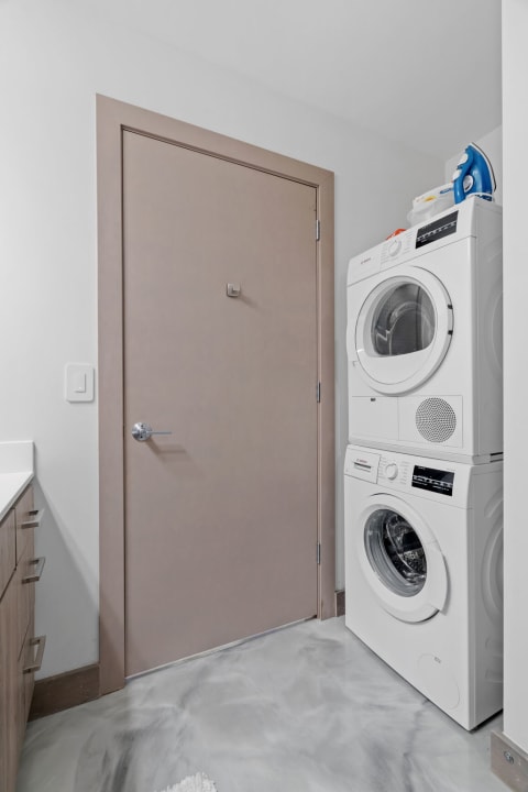 Interior view of a modern laundry room with stacked washer and dryer and storage cabinet.