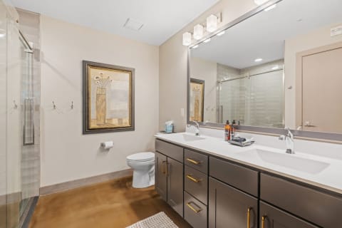 Modern bathroom featuring a double vanity, glass shower, and art piece on wall.