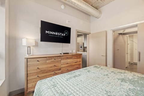A stylish bedroom with a mint-green bedspread and a large TV mounted on the wall.