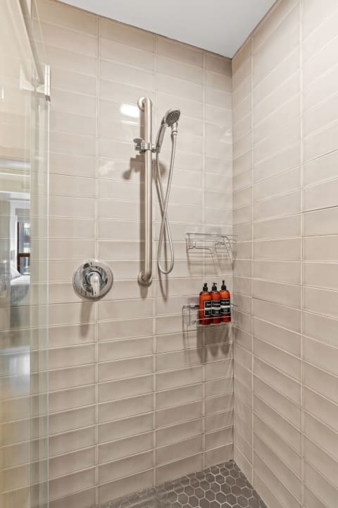 A contemporary shower area featuring beige tiled walls and a glass door.