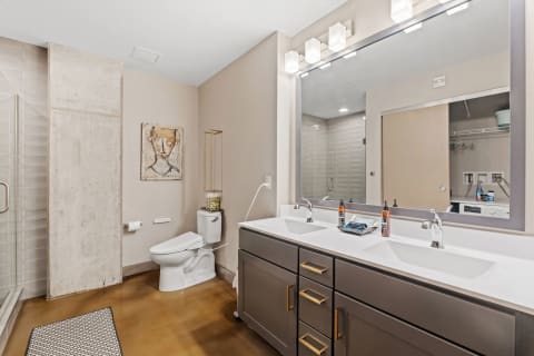A contemporary bathroom featuring a glass shower, double vanity with gold handles, and artistic wall decor.