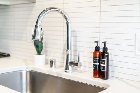 A stylish kitchen sink with chrome faucet and two labeled bottles of lotion and soap.