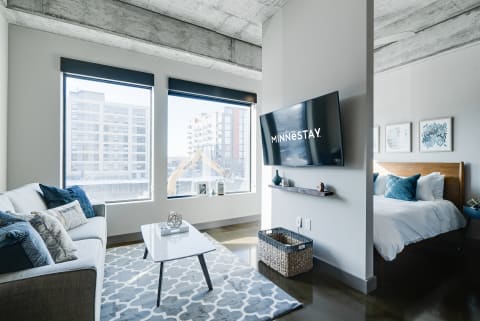 A modern living space with a gray sofa, white coffee table, and a bedroom visible in the background.