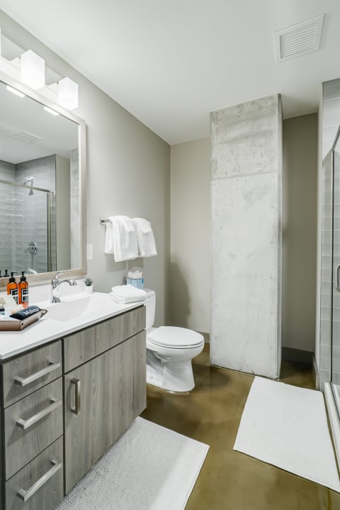 Modern bathroom featuring light wood vanity, concrete column, and grey tiled shower.
