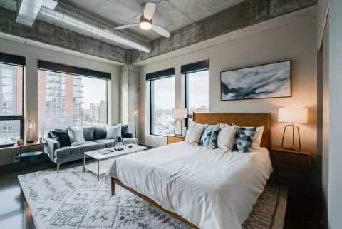 A contemporary bedroom featuring a large bed, a stylish couch, and large windows with an urban view.