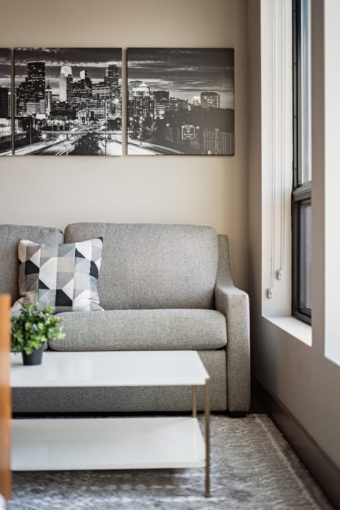 Cozy living room corner with a gray sofa, geometric pillow, and cityscape artwork.