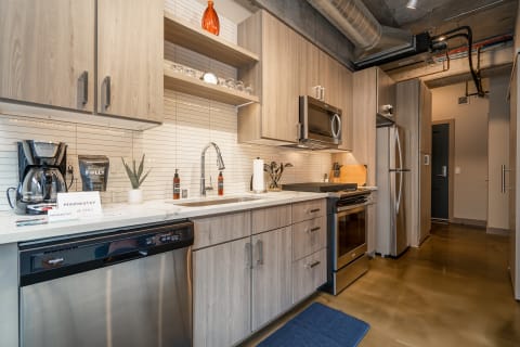 A modern kitchen featuring light wood cabinetry, stainless steel appliances, and a marble countertop.