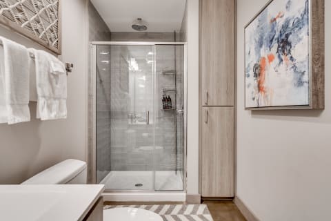 A modern bathroom with a walk-in shower, towels hanging, and vibrant artwork.
