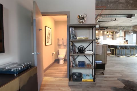 Interior of a modern apartment with an open layout, featuring a stylish shelf, turntable, and a glimpse of the bathroom.