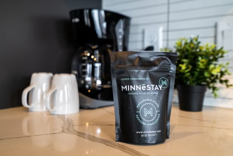 Coffee maker and bags on a marble countertop with white mugs in the foreground.