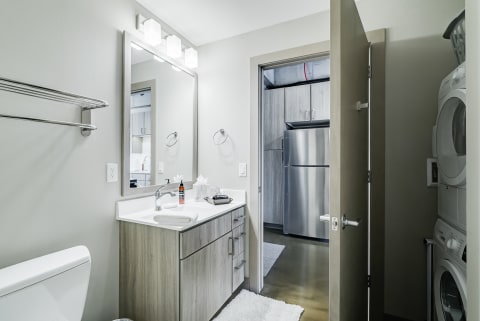 Interior view of a modern bathroom featuring a vanity, mirror, and doorway to a laundry area.
