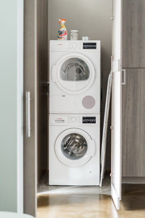 Stacked Bosch washer and dryer in a sleek laundry area with cleaning supplies on top.