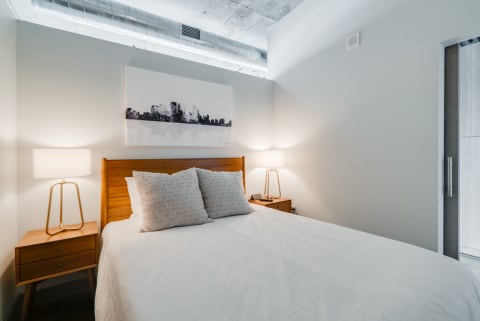 A contemporary bedroom featuring a white bed, wooden headboard, and warm lighting.