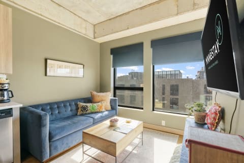 A contemporary living room with a blue sofa, coffee table, and urban views through large windows.