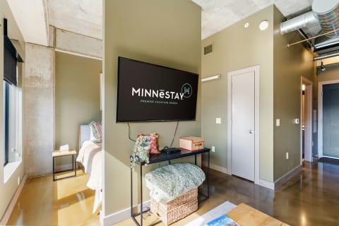 Modern living space with MINNēSTAY logo, featuring a flat-screen TV, bed, and decorative items.