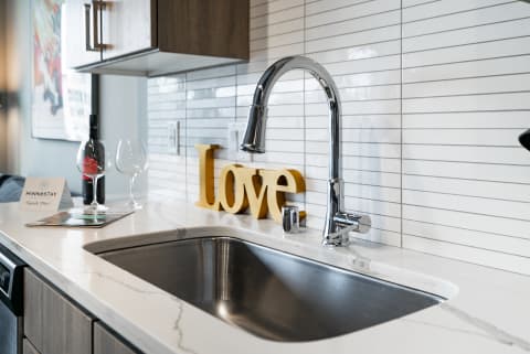 A contemporary kitchen sink with a chrome faucet, decorative letters spelling 'Love', wine glasses, and a bottle of wine.