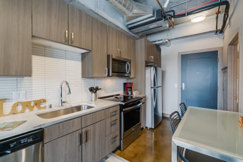 Modern kitchen with gray cabinets, stainless steel appliances, and a glass table.