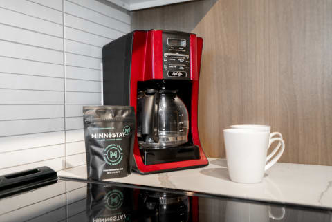 A red coffee maker, a coffee bag, and two white mugs on a kitchen countertop.
