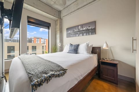 Cozy bedroom with a queen bed, decorative pillows, and large windows overlooking a city.