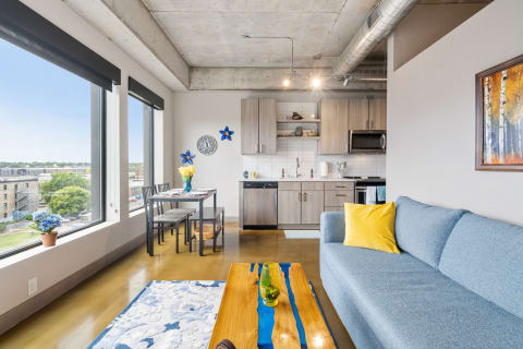 Interior of a stylish apartment featuring a blue sofa, dining area, and natural light from large windows.