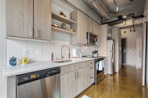A stylish kitchen featuring light wood cabinets and stainless steel appliances with decorative items on open shelves.