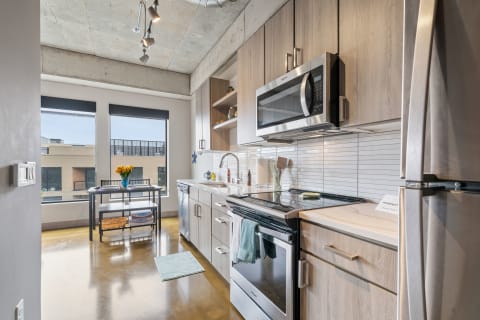 Modern kitchen with wooden cabinets, stainless steel appliances, and a view of the outside.