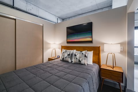 Contemporary bedroom featuring a grey quilted bed, geometric throw pillows, and an abstract artwork on the wall.