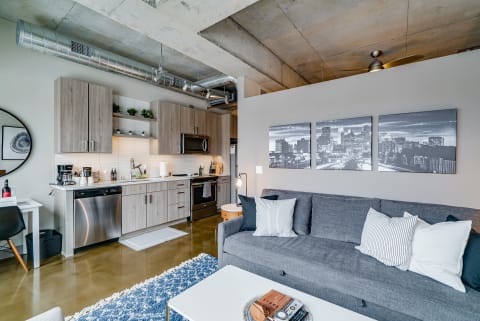 A stylish and modern studio apartment featuring a kitchen and living area with gray furniture and decorative elements.