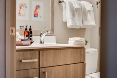 Modern bathroom featuring a wooden vanity, colorful wall art, and neatly arranged towels.