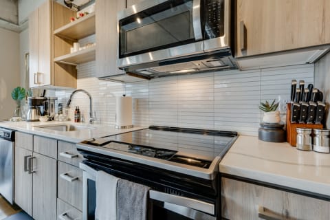 A contemporary kitchen featuring a black stovetop, light wood cabinets, and minimalist decor.