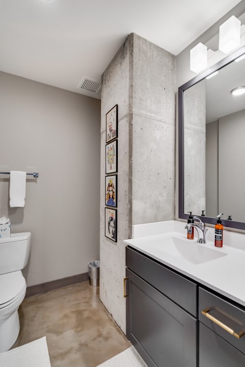 Modern bathroom featuring concrete wall, dark gray vanity, and framed art.