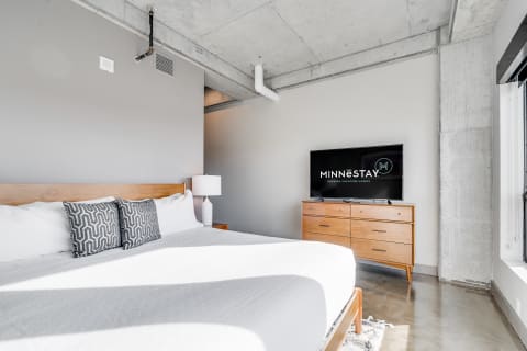 Contemporary bedroom with queen-sized bed, geometric pillows, and flat-screen TV.