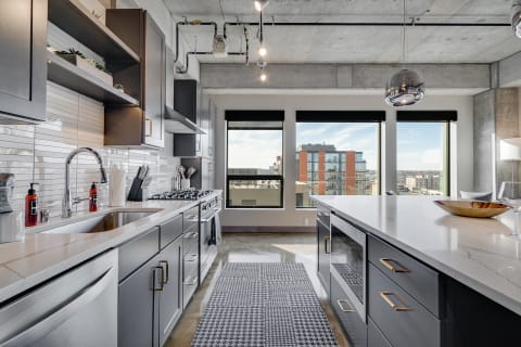 A modern kitchen with dark gray cabinetry, marble countertops, and large windows overlooking the city.