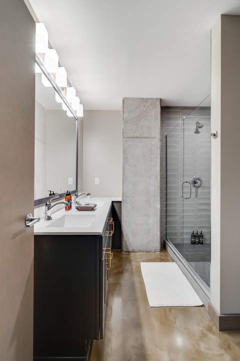 Modern bathroom with a double vanity, glass-enclosed shower, and polished concrete floor.
